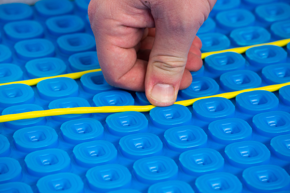 Underfloor heating cable being inserted into membrane